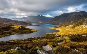Paysage photoréaliste du Connemara avec des lacs sinueux, montagnes escarpées et collines couvertes de bruyère sous un ciel nuageux.