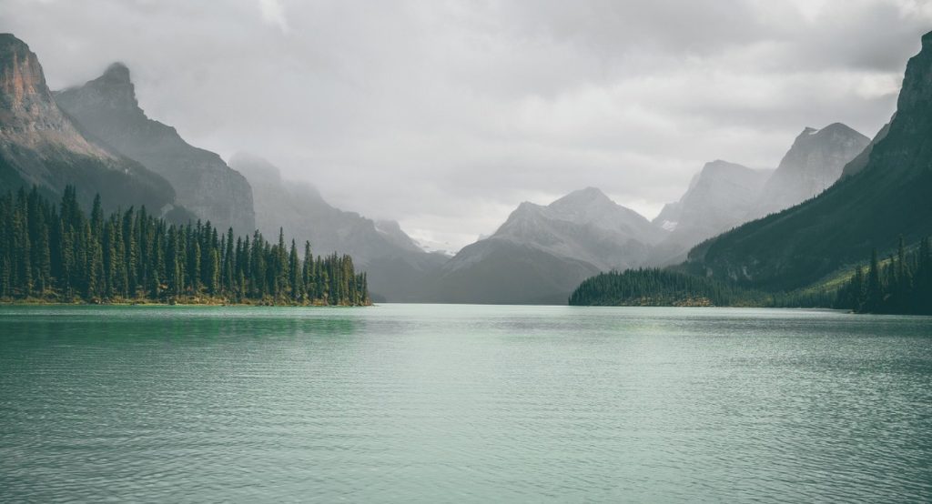 Lac de montagne calme entoure de sapins et de sommets brumeux