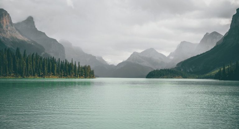 Lac de montagne calme entoure de sapins et de sommets brumeux